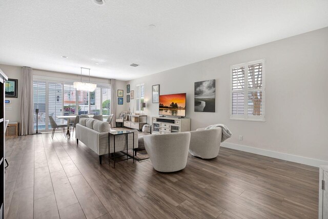 living room with dark wood-type flooring, an inviting chandelier, and a textured ceiling