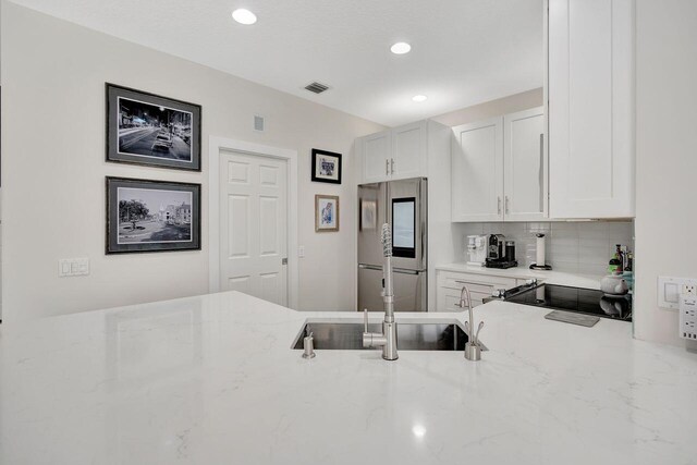 kitchen with decorative backsplash, stainless steel fridge, light stone countertops, and white cabinets