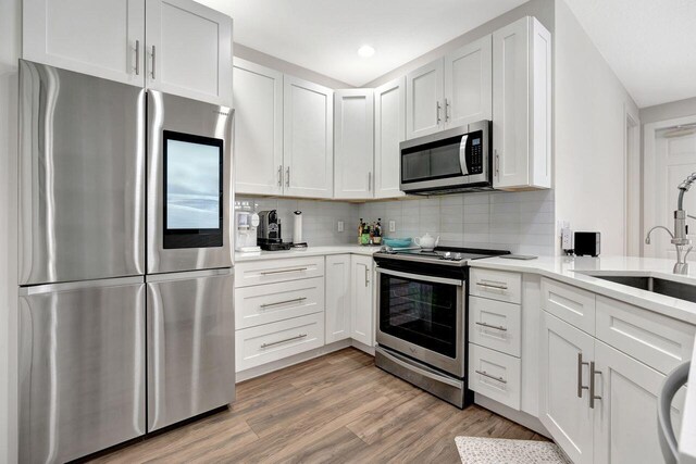 kitchen with appliances with stainless steel finishes, white cabinetry, sink, backsplash, and light wood-type flooring