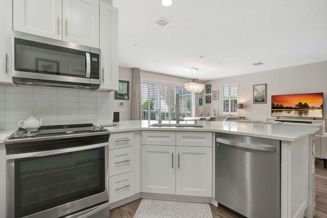 kitchen featuring sink, kitchen peninsula, white cabinets, stainless steel appliances, and backsplash