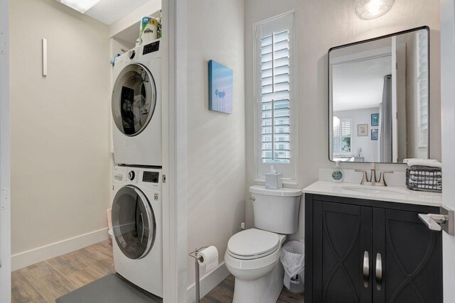 bathroom featuring vanity, stacked washer and clothes dryer, hardwood / wood-style floors, and toilet