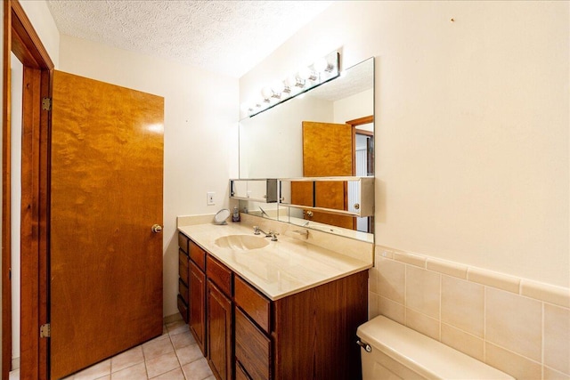 bathroom featuring a textured ceiling, tile patterned flooring, tile walls, toilet, and vanity