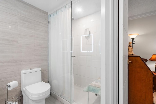 bathroom with toilet, a shower with door, and tile walls