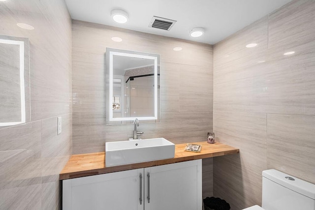 bathroom with toilet, vanity, and tile walls