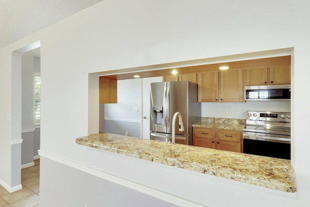 kitchen with kitchen peninsula, stainless steel appliances, light stone countertops, and light tile patterned floors