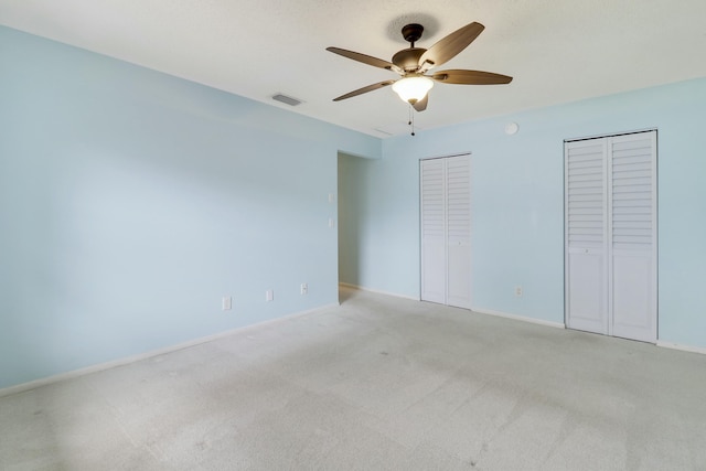 unfurnished bedroom with ceiling fan, light colored carpet, and two closets