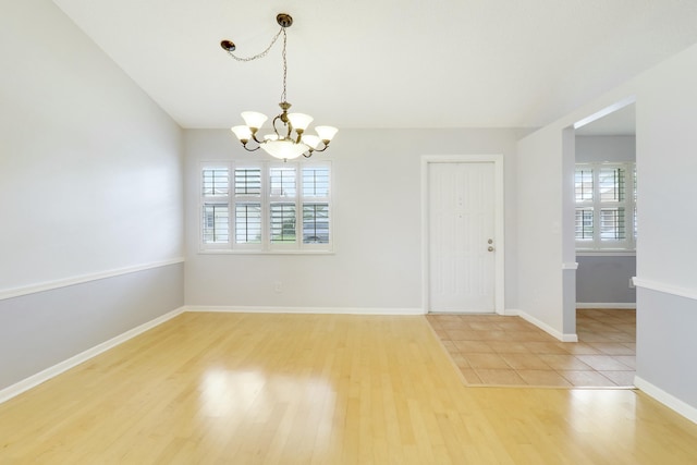 empty room featuring a healthy amount of sunlight, an inviting chandelier, and hardwood / wood-style flooring