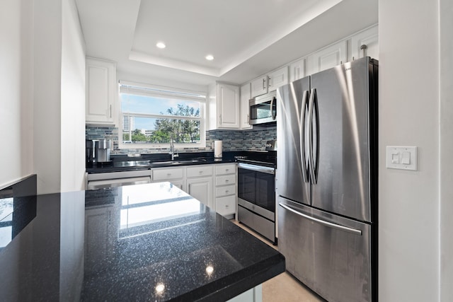 kitchen with appliances with stainless steel finishes, sink, white cabinets, and a tray ceiling