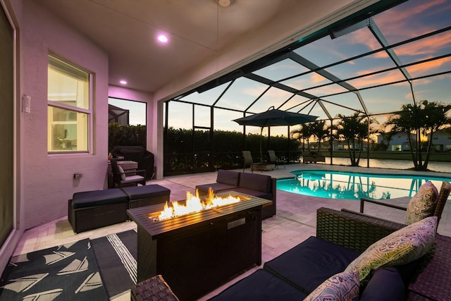 pool at dusk with grilling area, an outdoor living space with a fire pit, a patio, and glass enclosure