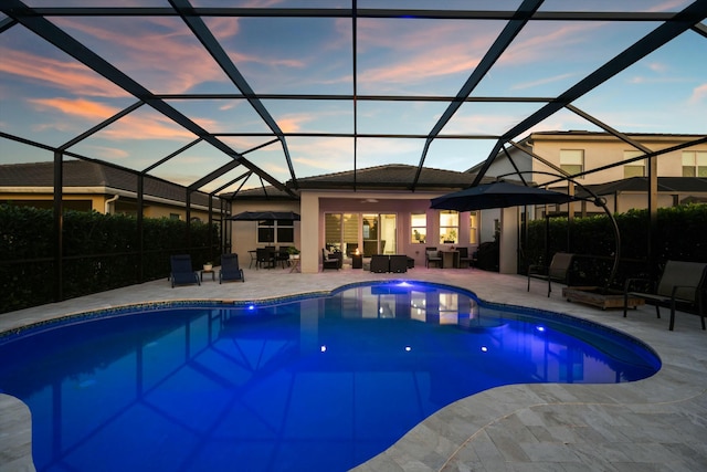 pool at dusk featuring a lanai and a patio