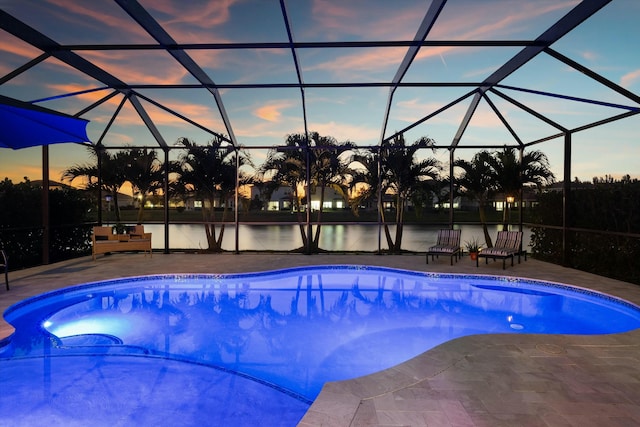 pool at dusk with a patio area, glass enclosure, and a water view