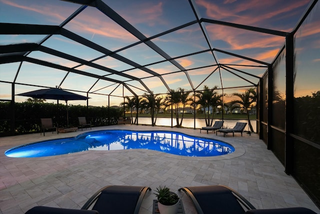 pool at dusk featuring a water view, a patio area, and glass enclosure