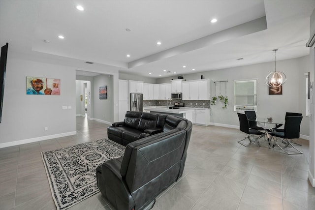 living room with sink, a tray ceiling, a chandelier, and light tile patterned flooring