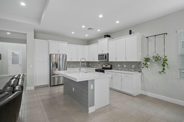 kitchen with white cabinetry, stainless steel appliances, an island with sink, sink, and backsplash