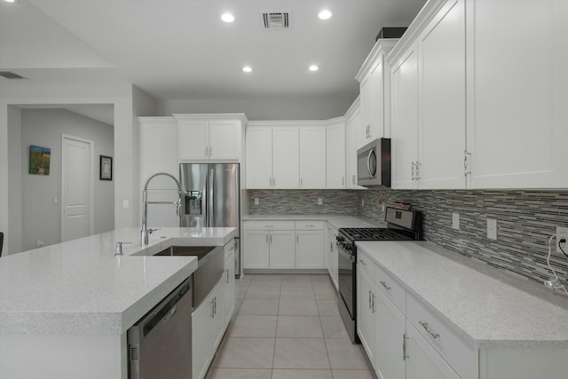 kitchen with decorative backsplash, light tile patterned flooring, appliances with stainless steel finishes, an island with sink, and white cabinets