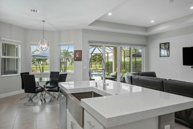 kitchen with white cabinets, decorative light fixtures, a kitchen island with sink, a chandelier, and a tray ceiling