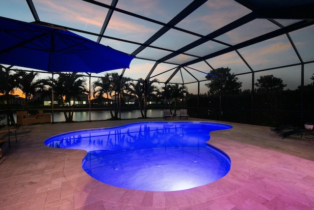 pool at dusk featuring glass enclosure, a water view, and a patio