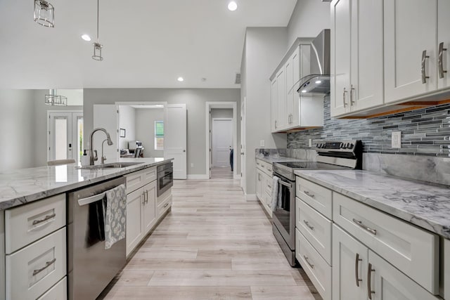 kitchen with light wood finished floors, decorative backsplash, appliances with stainless steel finishes, a sink, and wall chimney range hood