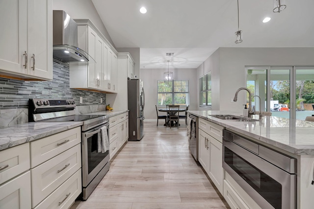 kitchen with white cabinetry, stainless steel appliances, decorative light fixtures, wall chimney range hood, and sink