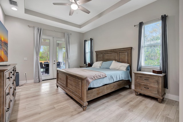 bedroom featuring visible vents, access to outside, french doors, light wood-type flooring, and a tray ceiling