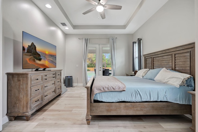 bedroom with access to exterior, a tray ceiling, french doors, light wood-style floors, and baseboards