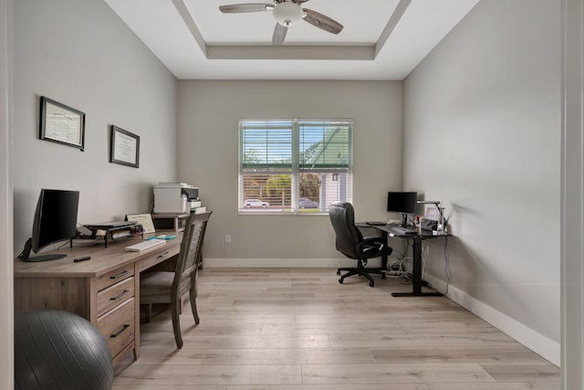 office area featuring light wood-style flooring, a tray ceiling, ceiling fan, and baseboards