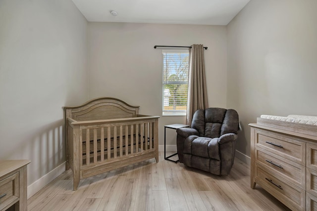 bedroom with light wood-style floors, baseboards, and a nursery area