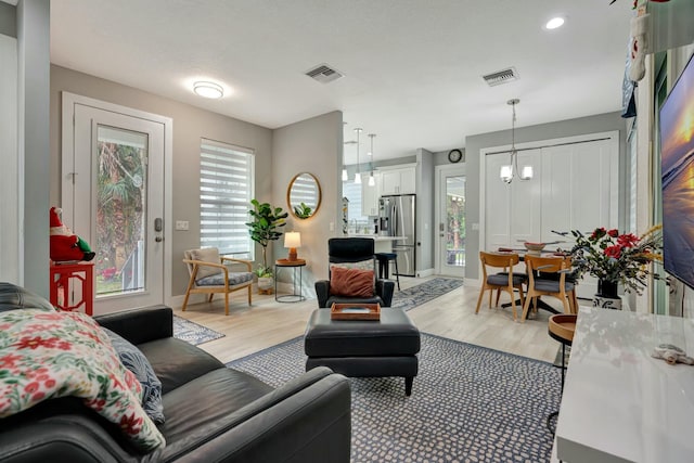 living room with light wood-type flooring, an inviting chandelier, baseboards, and visible vents