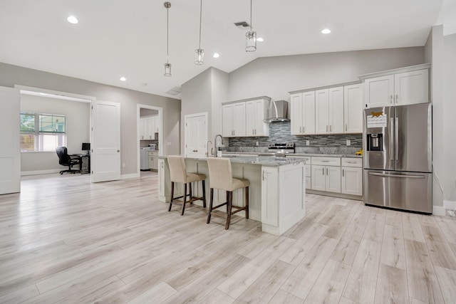 kitchen with tasteful backsplash, wall chimney exhaust hood, a breakfast bar, a kitchen island with sink, and stainless steel appliances