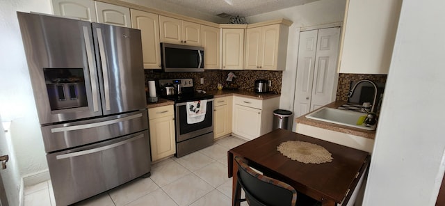 kitchen with a textured ceiling, backsplash, appliances with stainless steel finishes, cream cabinetry, and sink