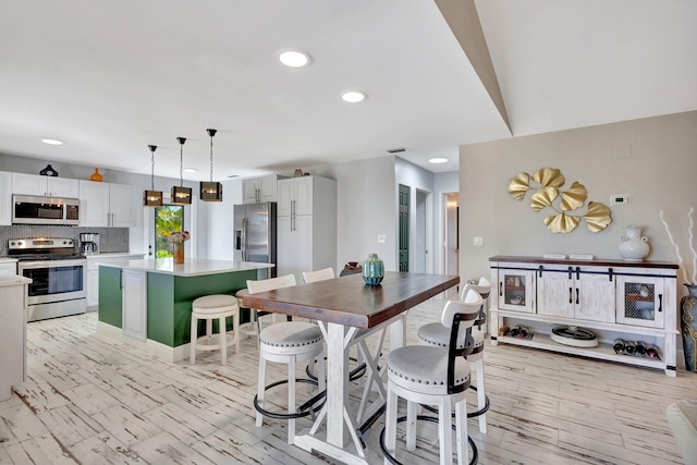 kitchen featuring stainless steel appliances, decorative light fixtures, a kitchen island, and white cabinets