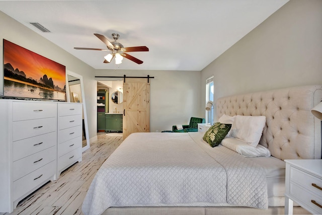 bedroom with a barn door, ceiling fan, and light hardwood / wood-style flooring