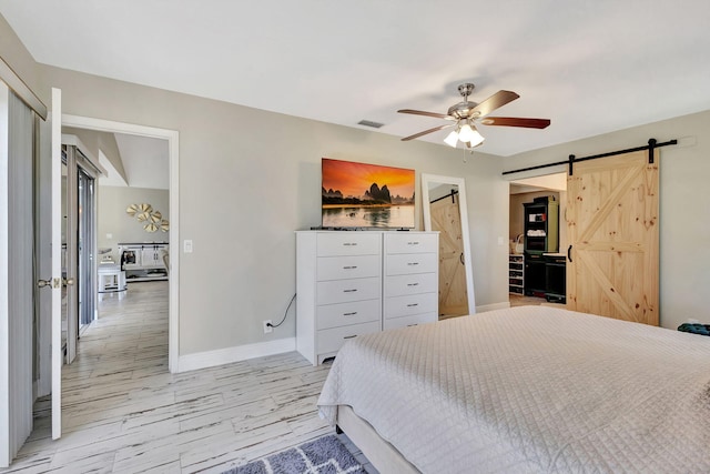 bedroom with a barn door, ceiling fan, and light hardwood / wood-style flooring