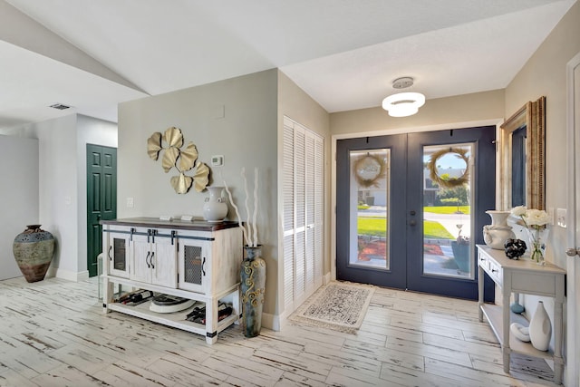 entryway featuring lofted ceiling, french doors, and light wood-type flooring