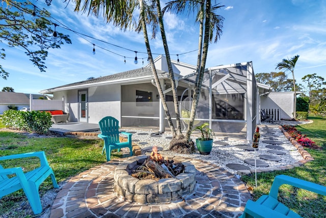 rear view of house with a lanai, a lawn, a patio area, and an outdoor fire pit