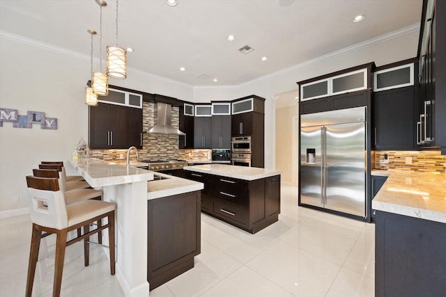 kitchen with decorative light fixtures, wall chimney range hood, kitchen peninsula, sink, and stainless steel appliances