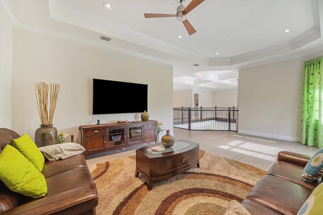 living room with a raised ceiling, light wood-type flooring, and crown molding