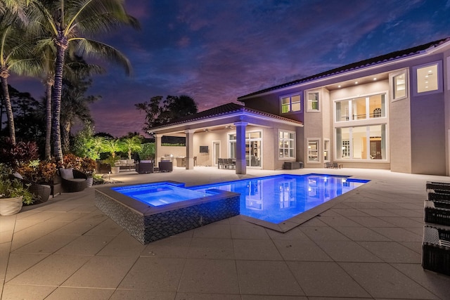 pool at dusk featuring a patio and an in ground hot tub