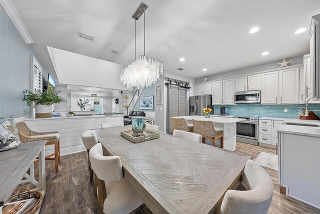 dining area featuring sink, crown molding, light hardwood / wood-style flooring, and a barn door