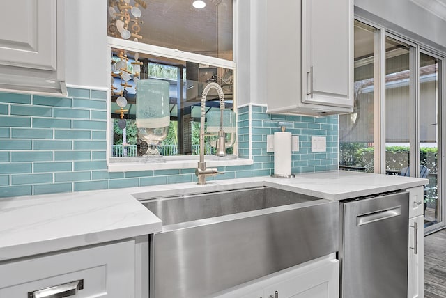 kitchen featuring light stone counters, dishwasher, decorative backsplash, white cabinets, and sink