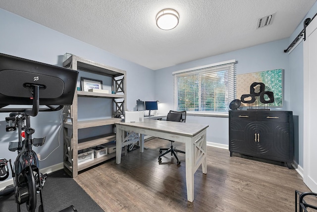 office featuring a textured ceiling, hardwood / wood-style flooring, and a barn door