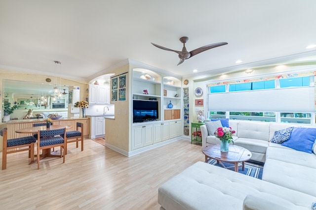 living room featuring ceiling fan, built in shelves, crown molding, and light hardwood / wood-style flooring