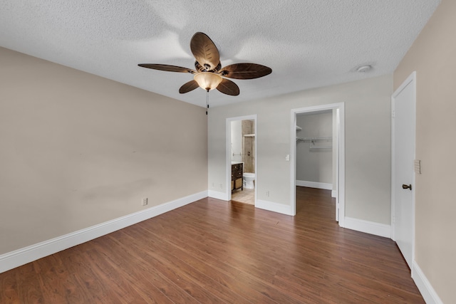 unfurnished bedroom featuring a walk in closet, dark wood-type flooring, a textured ceiling, and a closet