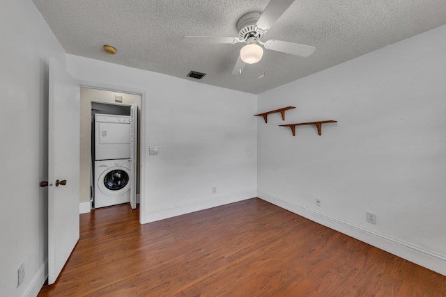 spare room with dark wood-type flooring, ceiling fan, stacked washer and clothes dryer, and a textured ceiling