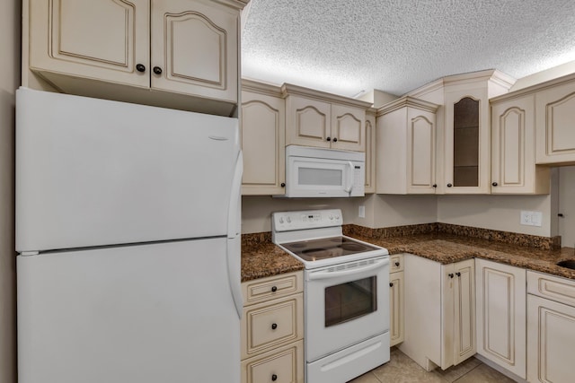 kitchen featuring white appliances, a textured ceiling, light tile patterned flooring, cream cabinetry, and dark stone counters