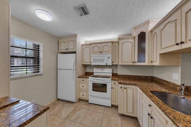 kitchen featuring sink, white appliances, light tile patterned floors, dark stone countertops, and cream cabinetry