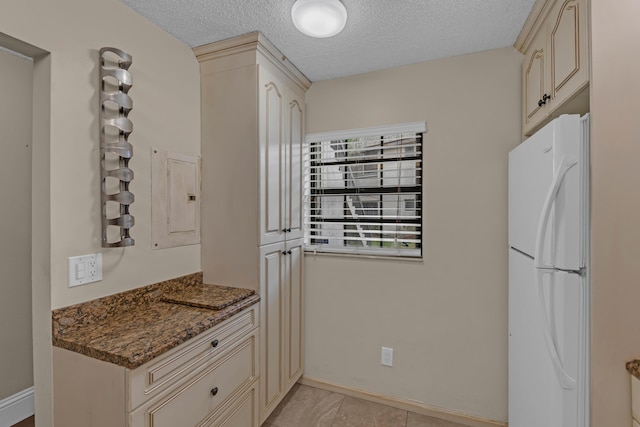 kitchen with dark stone counters, white refrigerator, electric panel, cream cabinets, and a textured ceiling