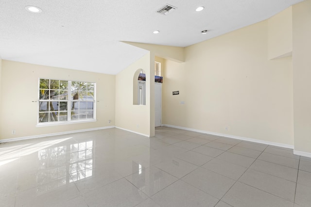 spare room featuring a textured ceiling, lofted ceiling, and light tile patterned flooring