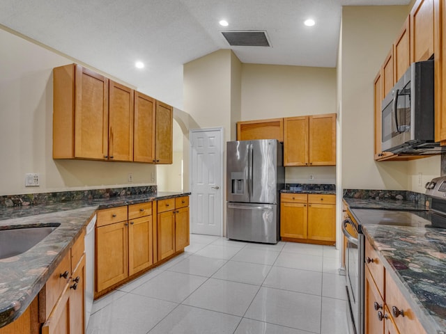 kitchen with appliances with stainless steel finishes, light tile patterned floors, sink, dark stone countertops, and high vaulted ceiling