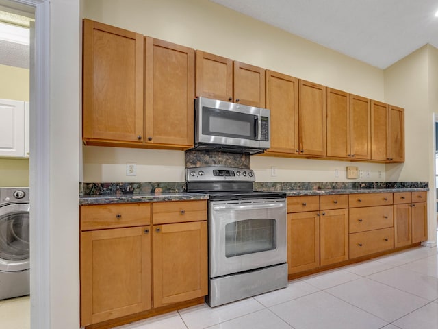 kitchen featuring washer / dryer, light tile patterned floors, a textured ceiling, dark stone countertops, and stainless steel appliances